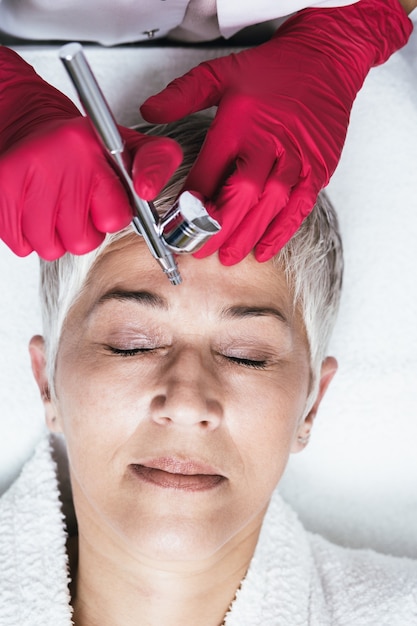 Photo une femme mûre reçoit des injections faciales rajeunissantes. elle est allongée calmement à la clinique. l'esthéticienne experte injecte du botox dans les rides de la femme.