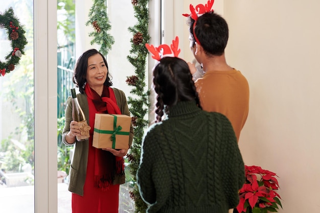 Femme mûre rendant visite à la famille de sa fille adulte et apportant du vin et un cadeau pour la fête de noël...