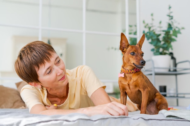 Une femme mûre se trouve sur le sol avec un petit chien pinscher nain