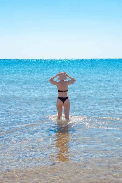 Une femme mûre avec une silhouette élancée dans un chapeau entre dans la mer Vacances d'été sur la côte Voyage et tourisme