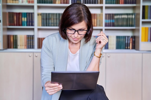 Femme mûre souriante d'affaires utilisant une tablette numérique dans le bureau de la bibliothèque