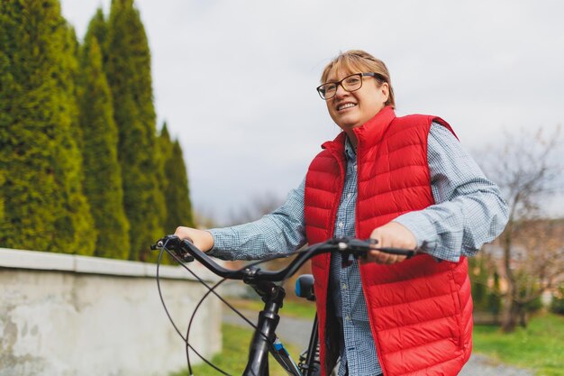 Femme mûre souriante d'âge moyen tenant un vélo avec ses mains sur l'herbe sur un champ vert Vacances d'été ou d'automne à la campagne et concept d'aventure