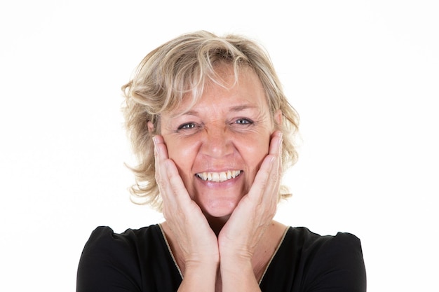 Femme mûre souriante avec la tête dans la main sur les joues en fond de studio blanc