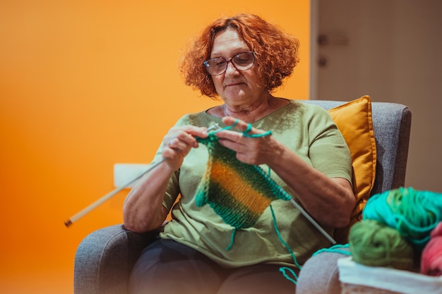 Femme mûre tenant des aiguilles à tricoter et tricoter à la maison