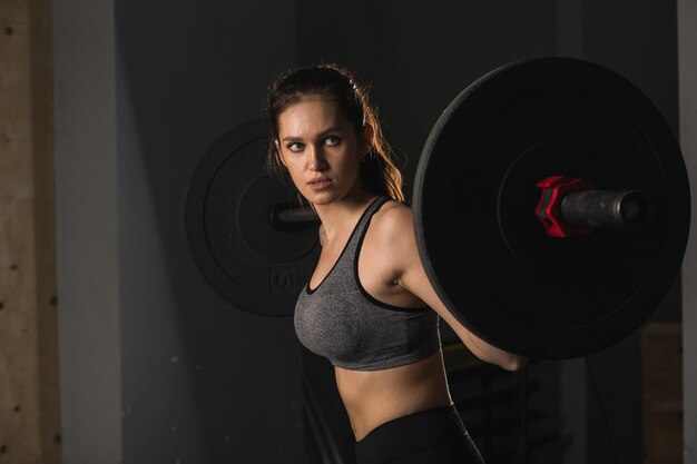 Femme musclée dans un gymnase faisant des exercices de poids lourds avec haltères