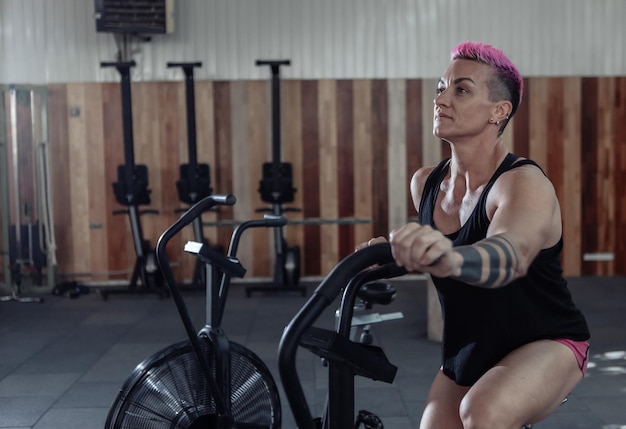 Photo femme musclée exerçant sur vélo à air. entraînement de fitness à vélo. femme athlétique utilisant un entraînement cardio-vélo à air. entraînement fonctionnel croisé.