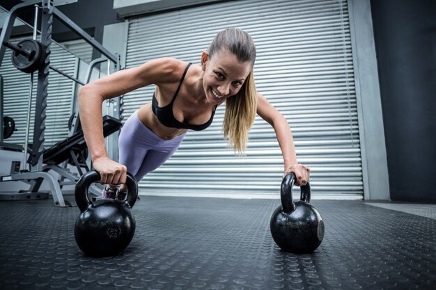 Femme musclée faisant des pompes avec des kettlebells