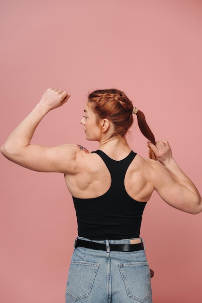 Photo une femme musclée sportive en t-shirt et en jean montrant un dos fort sur un fond rose