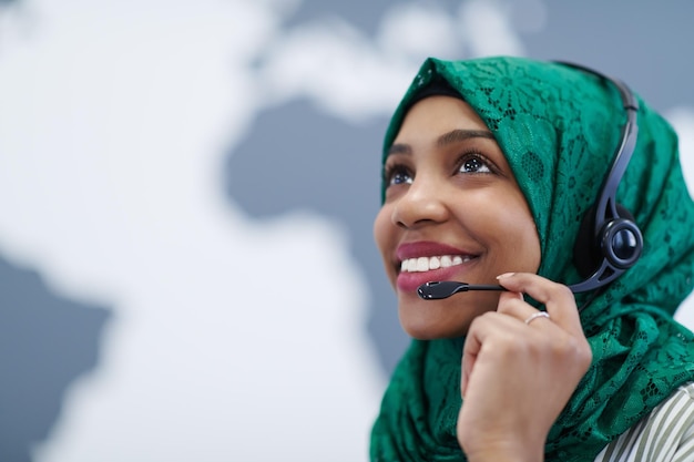 Femme musulmane africaine avec écharpe hijab verte représentante de la clientèle femme d'affaires avec casque téléphonique aidant et soutenant en ligne avec le client dans un centre d'appels moderne