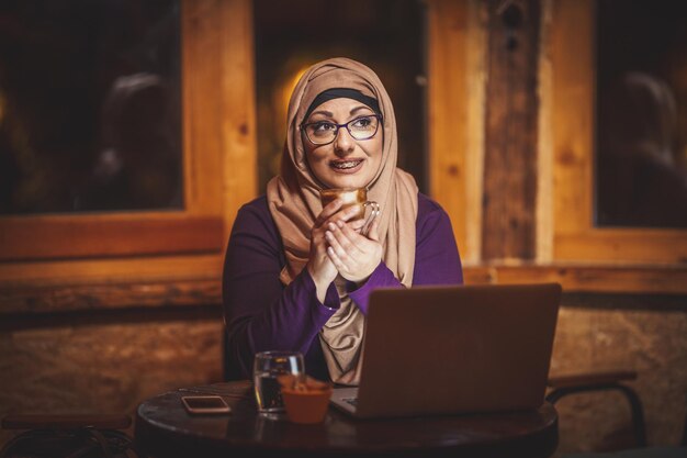 Femme musulmane d'âge moyen portant du café et travaillant sur un ordinateur portable