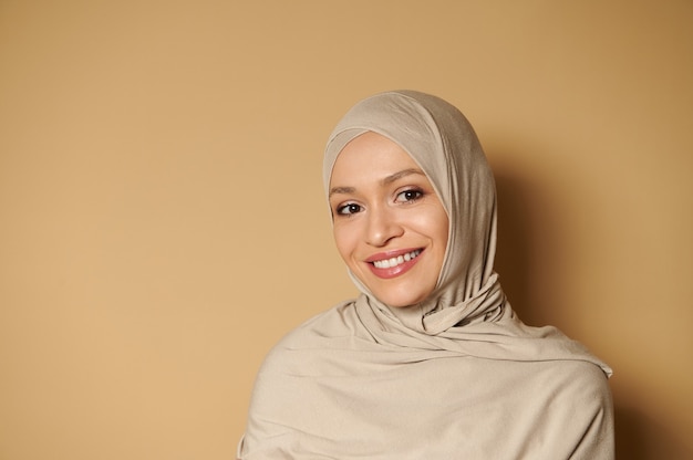 Femme musulmane arabe portant le hijab à l'avant tout en posant avec un beau sourire à pleines dents sur une surface beige avec espace copie