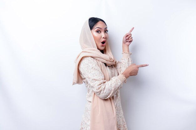 Femme musulmane asiatique choquée pointant vers l'espace de copie à côté d'elle isolé par fond blanc