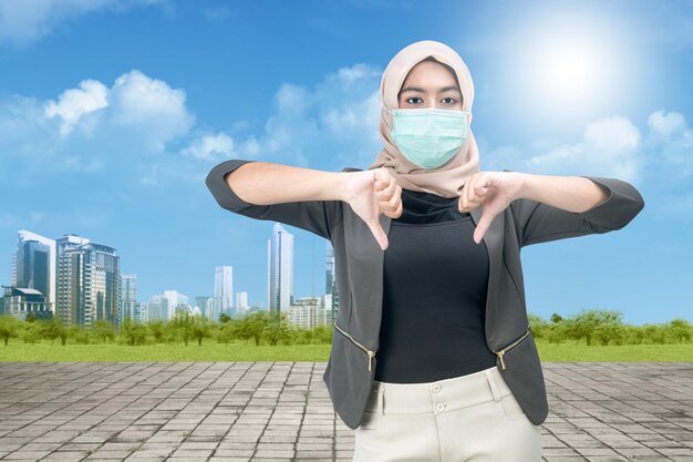 Femme musulmane asiatique dans un foulard et portant un masque facial debout montrant le signe du pouce vers le bas