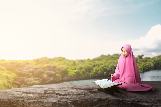 Femme musulmane asiatique dans un voile assis et lisant le Coran à l'extérieur