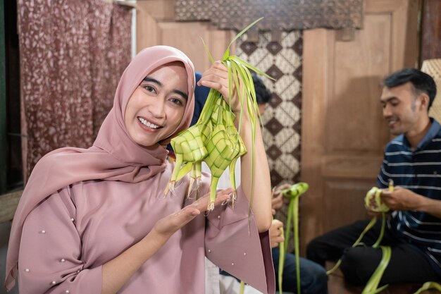 Femme musulmane asiatique excitée faisant du riz ketupat avec des feuilles de coco pendant le ramadan kareem se préparant à la célébration de l'Aïd fitri moubarak