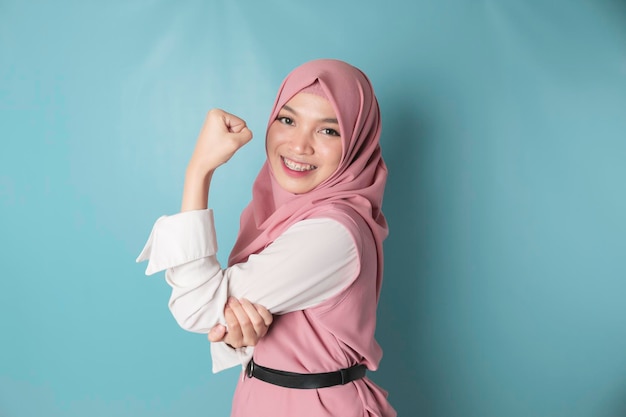 Femme musulmane asiatique excitée portant un hijab rose montrant un geste fort en levant les bras et les muscles en souriant fièrement