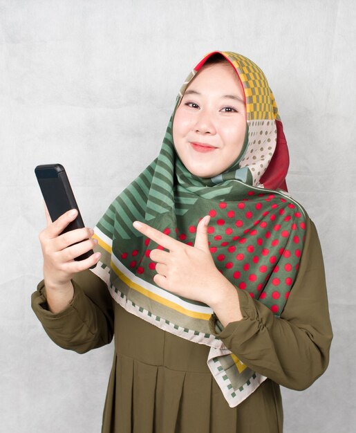 La femme musulmane asiatique fait la promotion d'un produit en pointant sur un téléphone portable