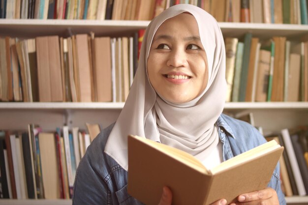 Femme musulmane asiatique qui pense en lisant un livre concept d'apprentissage de l'éducation étudiant dans la bibliothèque