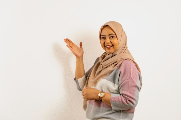 Femme musulmane asiatique souriante portant un hijab présentant quelque chose sur son côté droit avec la main