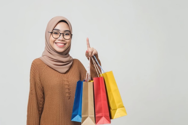 Une femme musulmane asiatique sourit en montrant des sacs à courses sur fond blanc.