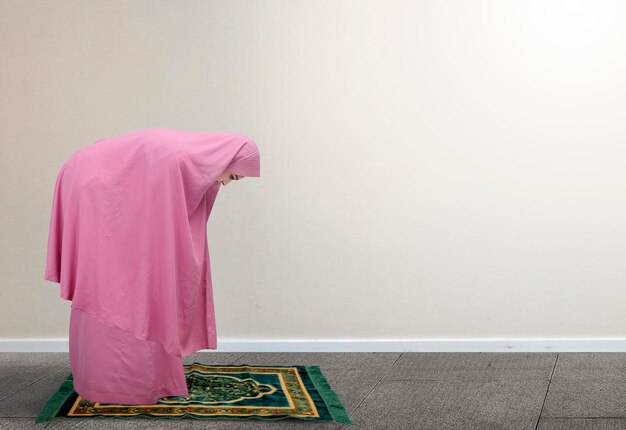 Femme musulmane asiatique en voile en position de prière salat avec fond de mur blanc