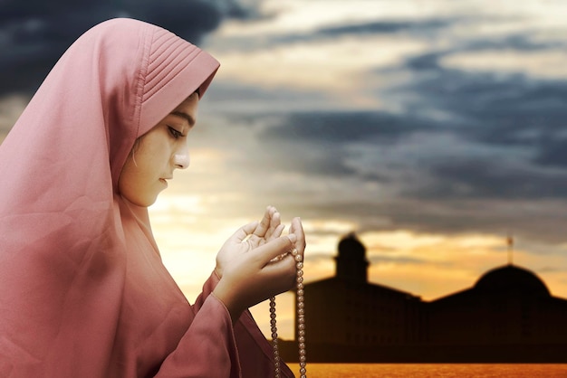 Femme musulmane asiatique en voile priant avec des perles de prière sur ses mains avec le fond de scène dramatique