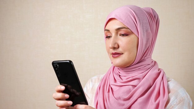 Une femme musulmane dans une écharpe avec un téléphone dans les mains tape du texte.