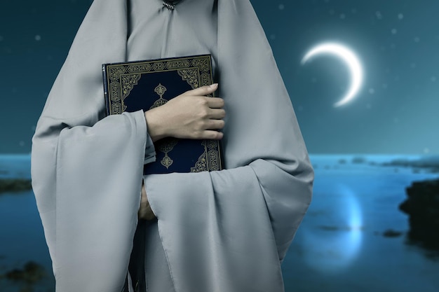 Femme musulmane dans un voile debout et tenant le Coran avec le fond de scène de nuit