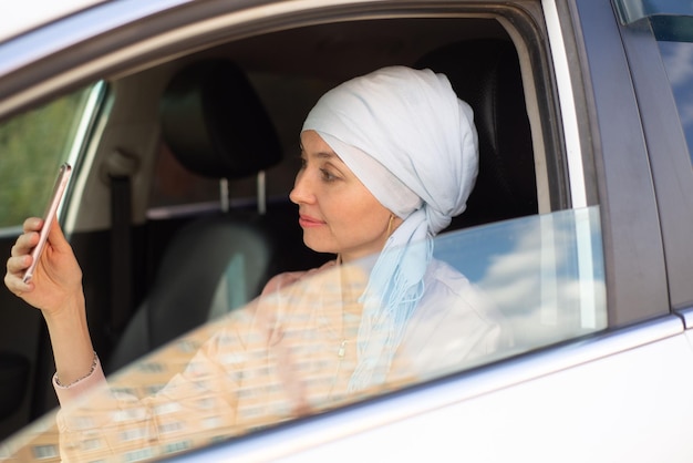 Une femme musulmane est assise dans la voiture moderne et fait du selphie par téléphone portable