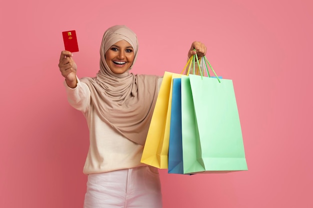 Femme musulmane excitée en hijab posant avec des sacs à provisions et une carte de crédit