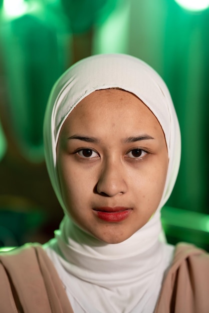 Une femme musulmane avec un foulard blanc et des vêtements blancs est assise au milieu d'une pièce verte sans maquillage