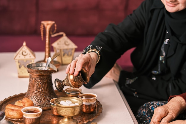 Une femme musulmane heureuse en hijab servant du café turc à sa vieille mère après le dessert à la maison pendant l'Aid Mubarak Ramadan