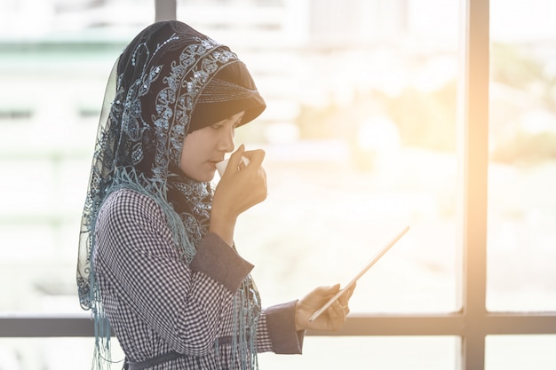 Femme musulmane islamique boit du café en regardant une tablette