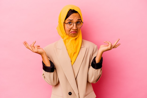 Femme musulmane jeune entreprise isolée sur fond rose doutant et haussant les épaules dans le geste de questionnement.