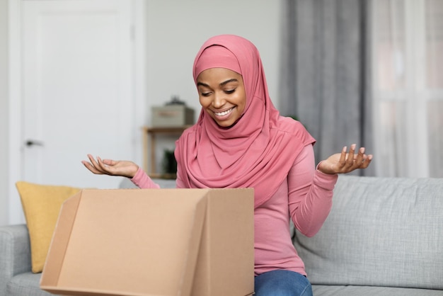 Femme musulmane noire ravie déballant la boîte de livraison client satisfait ouvrant le colis à la maison