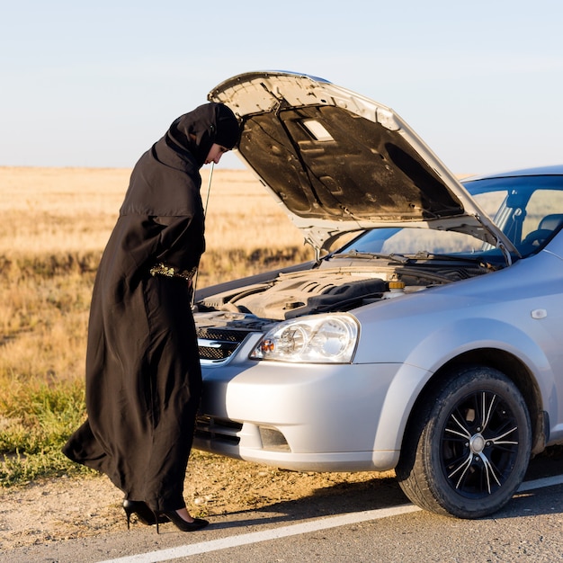 Femme musulmane près du capot ouvert de la voiture sur route vide