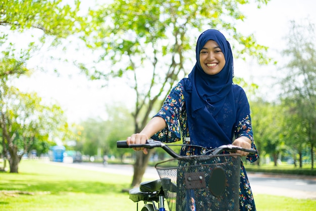 Femme musulmane tenant un vélo dans le jardin.