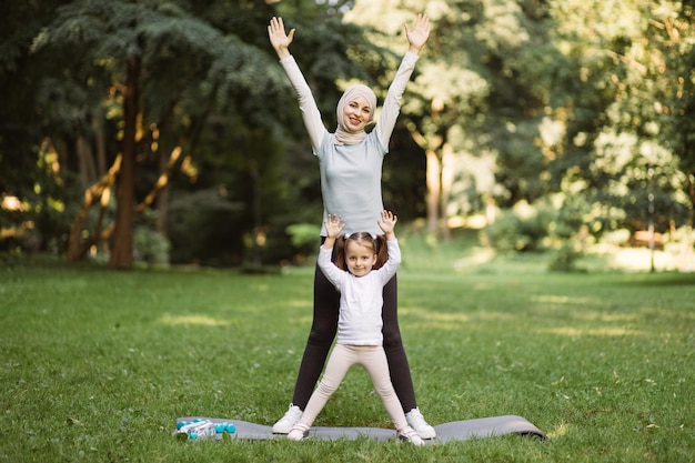 Femme musulmane en vêtements de sport et sa jolie fille faisant des exercices de sport dans le parc