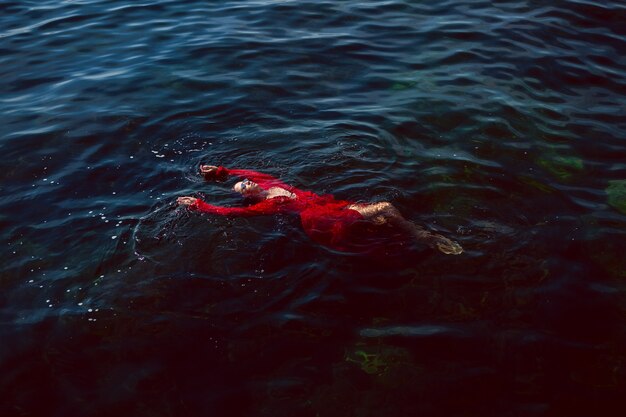 Femme nage dans la mer dans une robe longue rouge avec des lunettes de soleil en été
