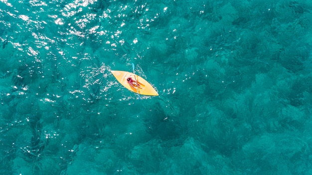 Femme nage sur un kayak de sport dans un océan exotique de turquoise clair.