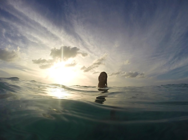 Photo une femme nageant dans la mer contre le ciel au coucher du soleil