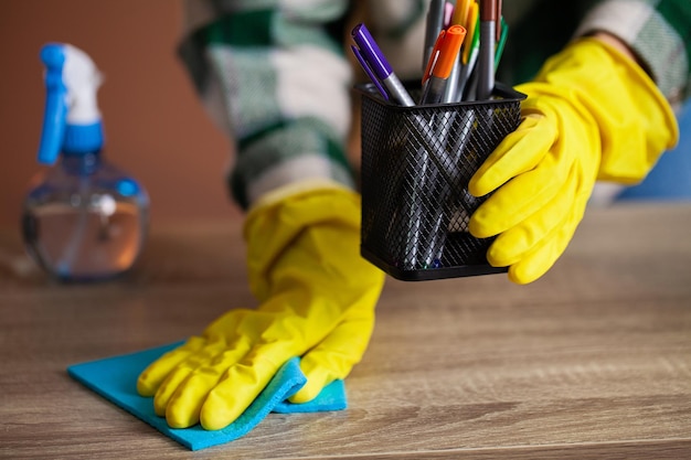 La femme nettoie le bureau dans les gants jaunes essuie la poussière du bureau