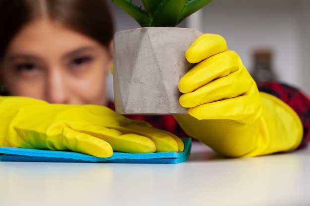 La femme nettoie le bureau dans les gants jaunes essuie la poussière du bureau