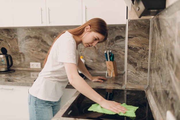 Une femme nettoie dans la cuisine avec un chiffon dans les mains.