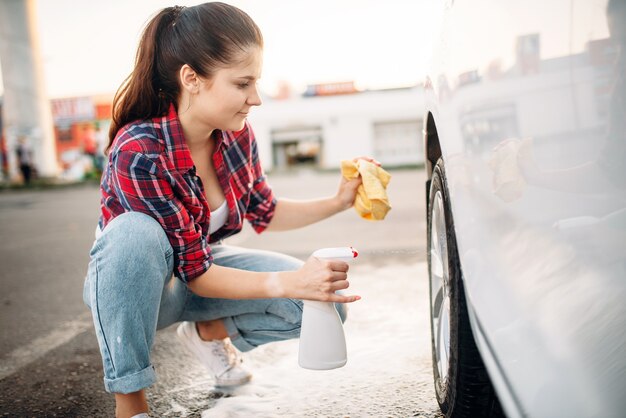 Femme nettoie le disque de roue de la voiture avec un spray, un lave-auto. Dame sur le lavage d'automobiles en libre-service. Nettoyage de véhicules extérieurs le jour d'été