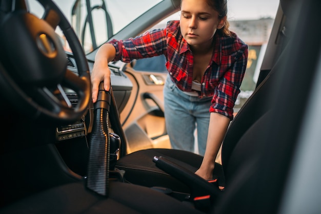 Femme nettoie l'intérieur de la voiture avec aspirateur, lave-auto. Dame avec aspirateur sur le lavage automobile en libre-service. Nettoyage de véhicules extérieurs le jour d'été