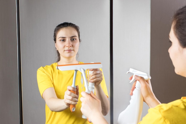 Une femme nettoie le miroir avec un distributeur et un nettoyant pour vitres