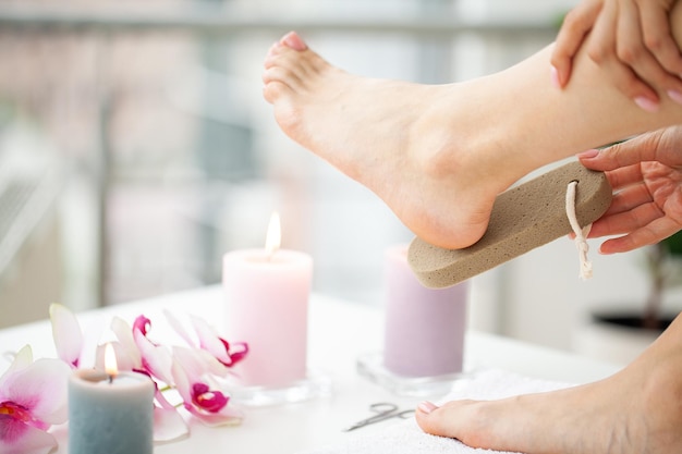 La femme nettoie le talon du pied avec de la pierre ponce.