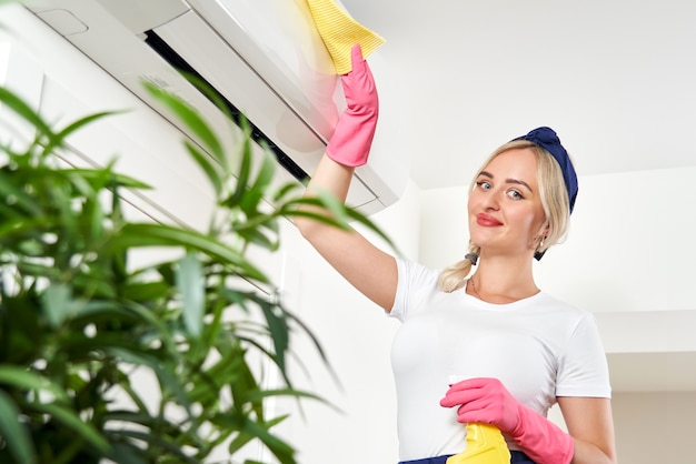 Femme de nettoyage du climatiseur avec un chiffon. Service de nettoyage ou concept de femme au foyer