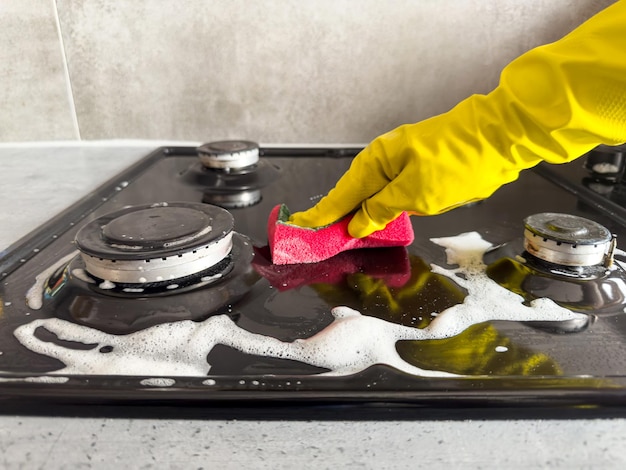 Femme nettoyant un chiffon éponge avec de la mousse blanche et du détergent lavant un poêle à gaz de cuisine